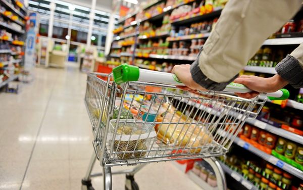 Shopper pushing a trolley down a supermarket aisle lined with shelves of boxed and canned food