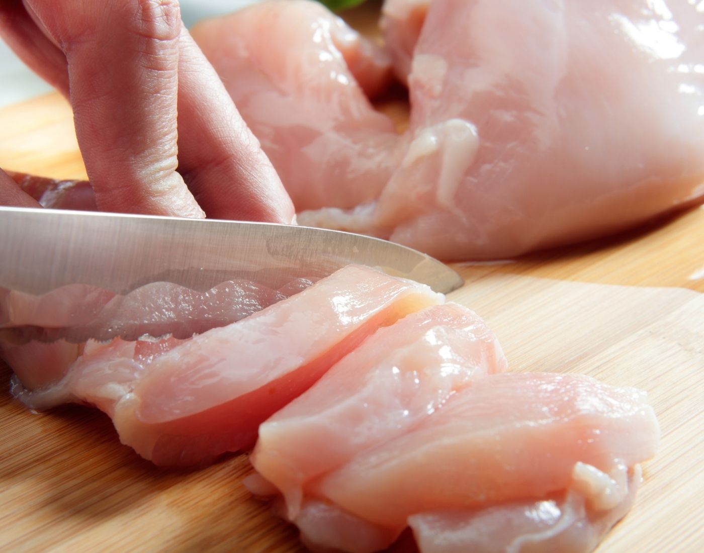 Raw chicken breast being cut into pieces on a wooden chopping board