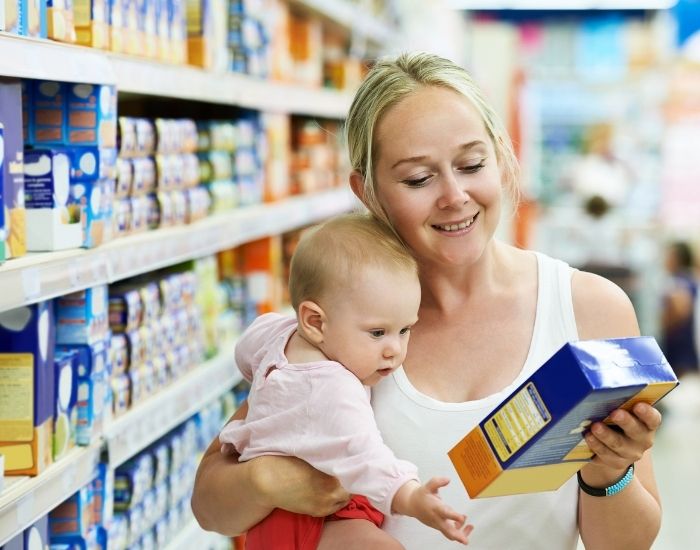 Mother holding a baby is reading a food packaging label in a supermarket aisle