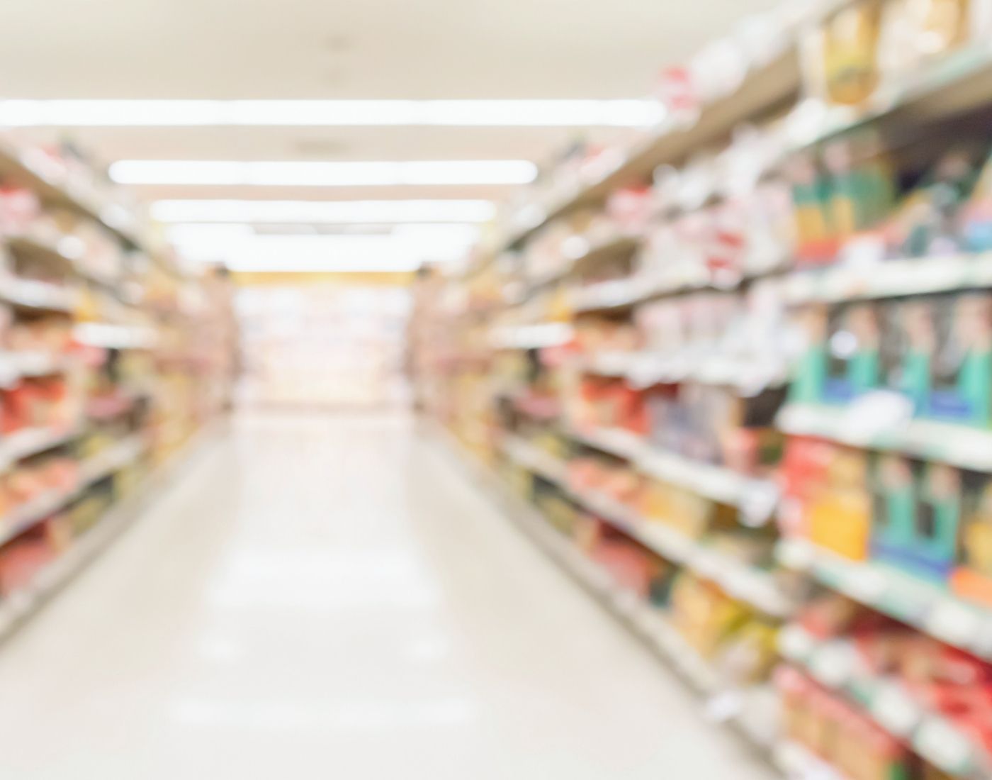 Blurred view of a brightly lit supermarket aisle with shelves stocked on both sides, suggesting a clean and well-maintained retail environment.