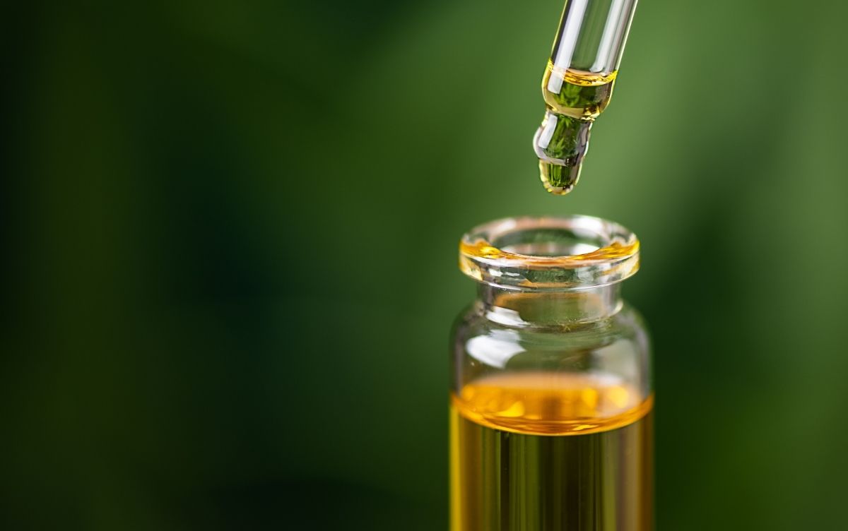 A dropper dispensing liquid into a small bottle set against a blurred green background