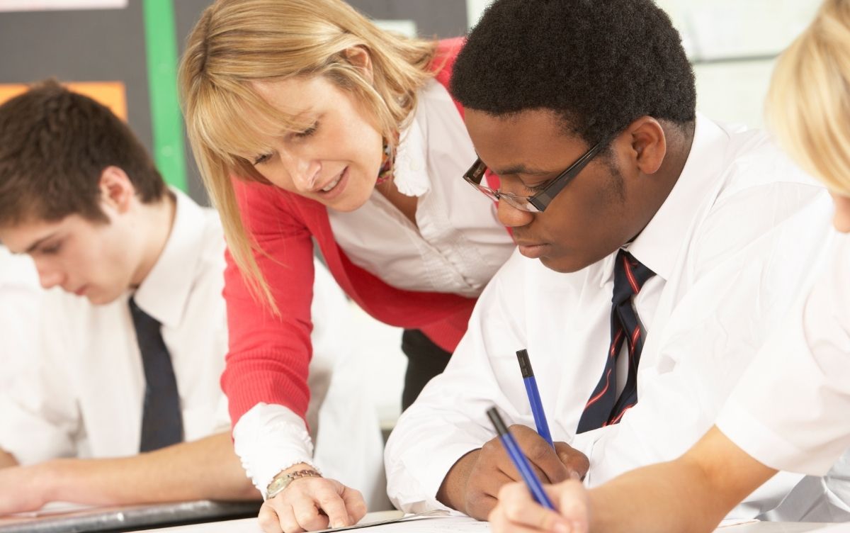 Teacher speaking to secondary school aged boy in a classroom.