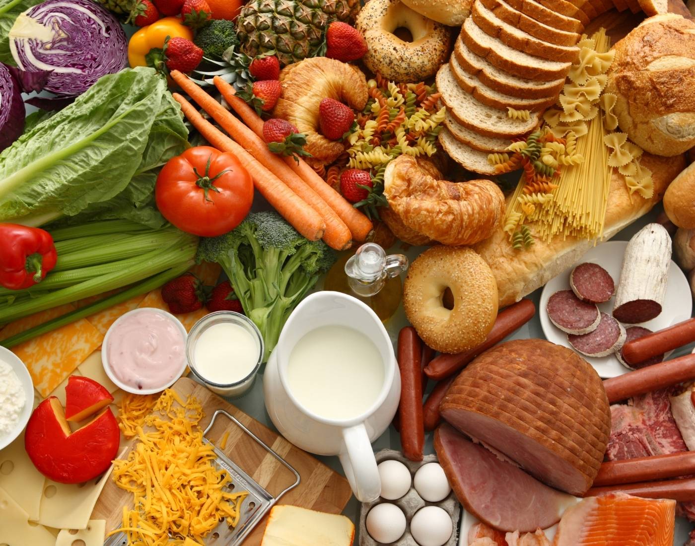 Range of foods laid out on a table including fruit, vegetables, bread, meat and dairy products.