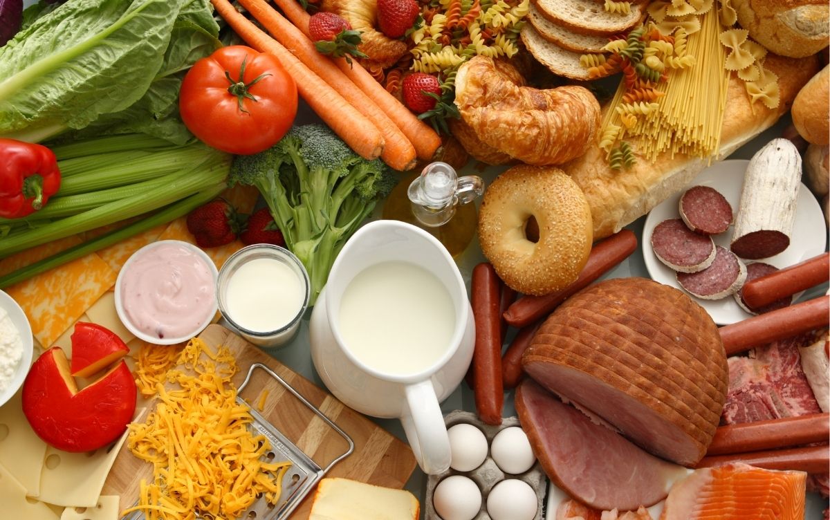 Range of foods laid out on a table including fruit, vegetables, meat, dairy and bread products.